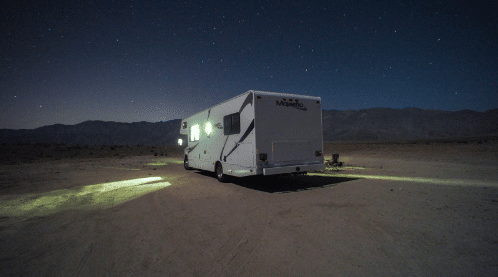 RV parked in the desert at night with a mountain range in the background.