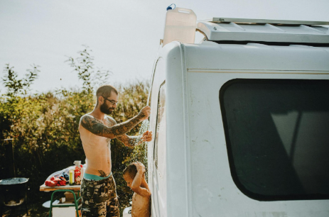 Man and son using a RV outdoor shower to cool off in the hot summer day.