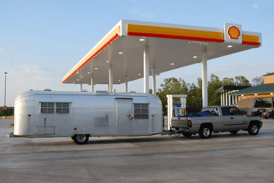 Grey pickup truck hauling a travel trailer to a gas station in Iowa.